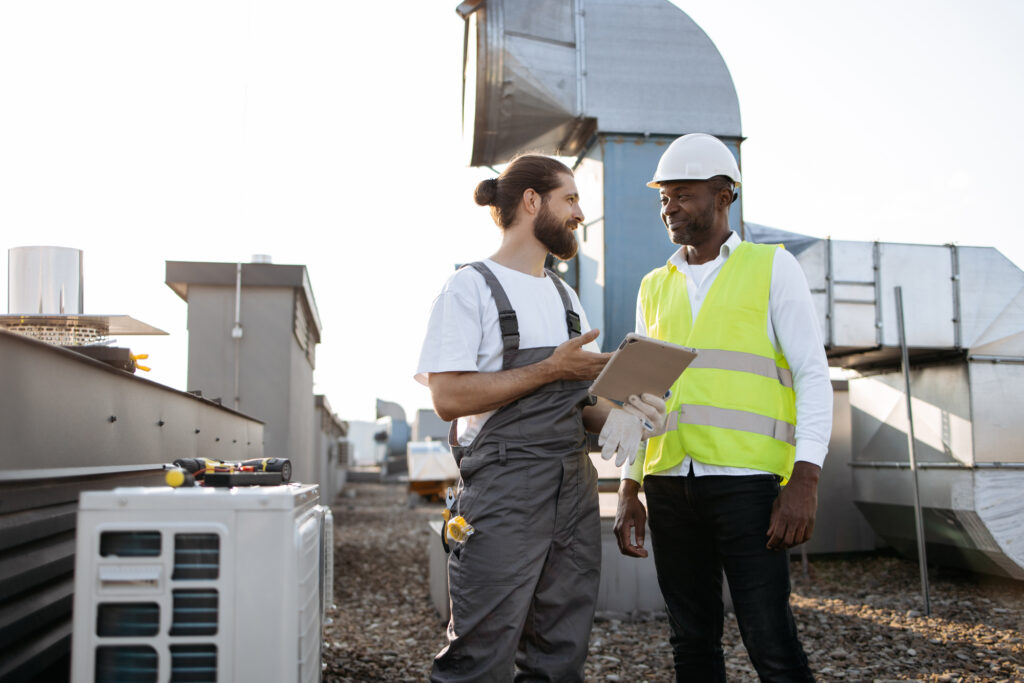 Workers looking at tablet and servicing conditioners outdoor